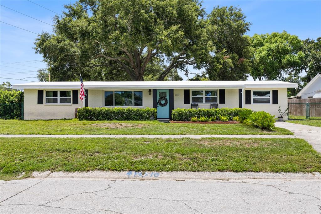 A single-story, light-colored brick house features a flat roof, black shutters, and a front lawn — 2287 MANOR BOULEVARD N, CLEARWATER, FL