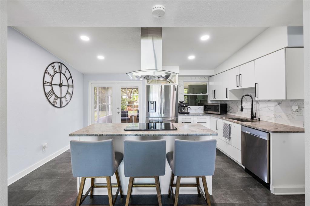 A modern kitchen features a central island with bar seating, white cabinetry, and stainless appliances — 2287 MANOR BOULEVARD N, CLEARWATER, FL