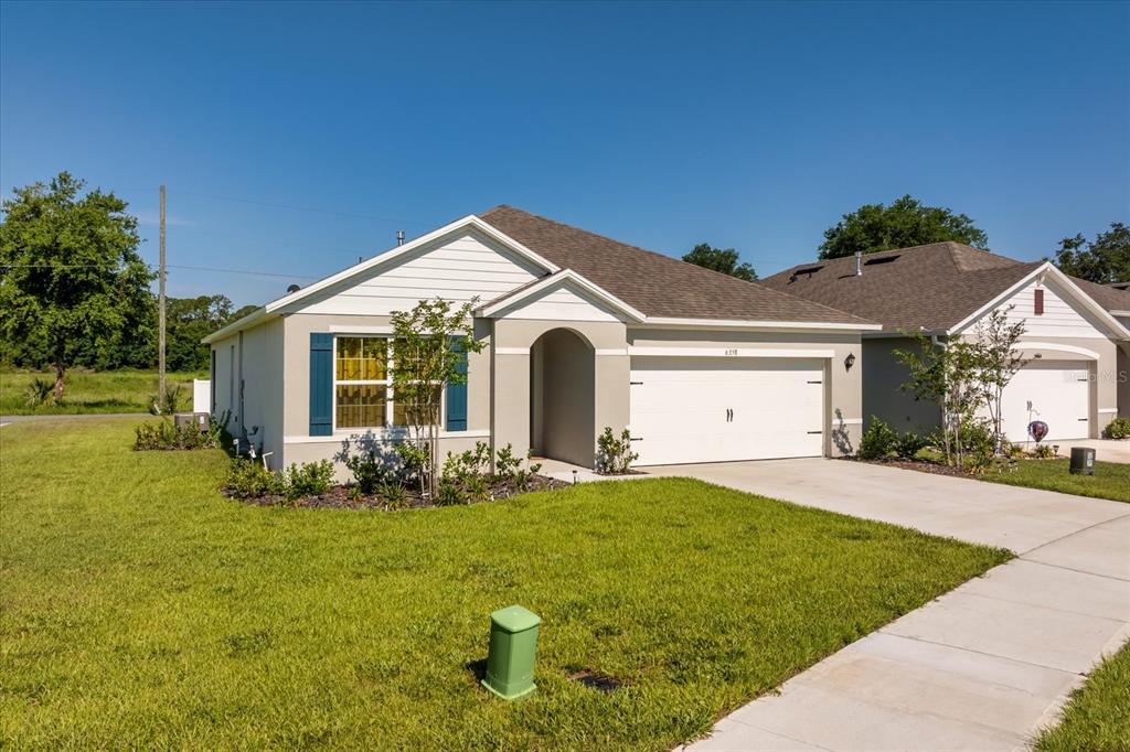 A single-story suburban house with a beige stucco exterior, a two-car garage, and blue shutters — 6358 SANDERS GROVE CIRCLE, OKAHUMPKA, FL
