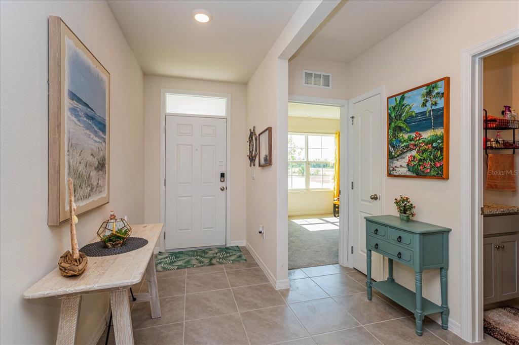 A tiled entryway features a white front door, two console tables, and wall-mounted artwork — 6358 SANDERS GROVE CIRCLE, OKAHUMPKA, FL