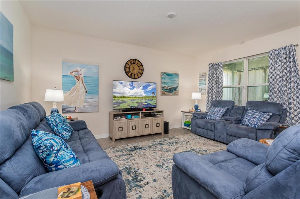 A living room features blue reclining sofas, a television on a console, and coastal decor — 6358 SANDERS GROVE CIRCLE, OKAHUMPKA, FL