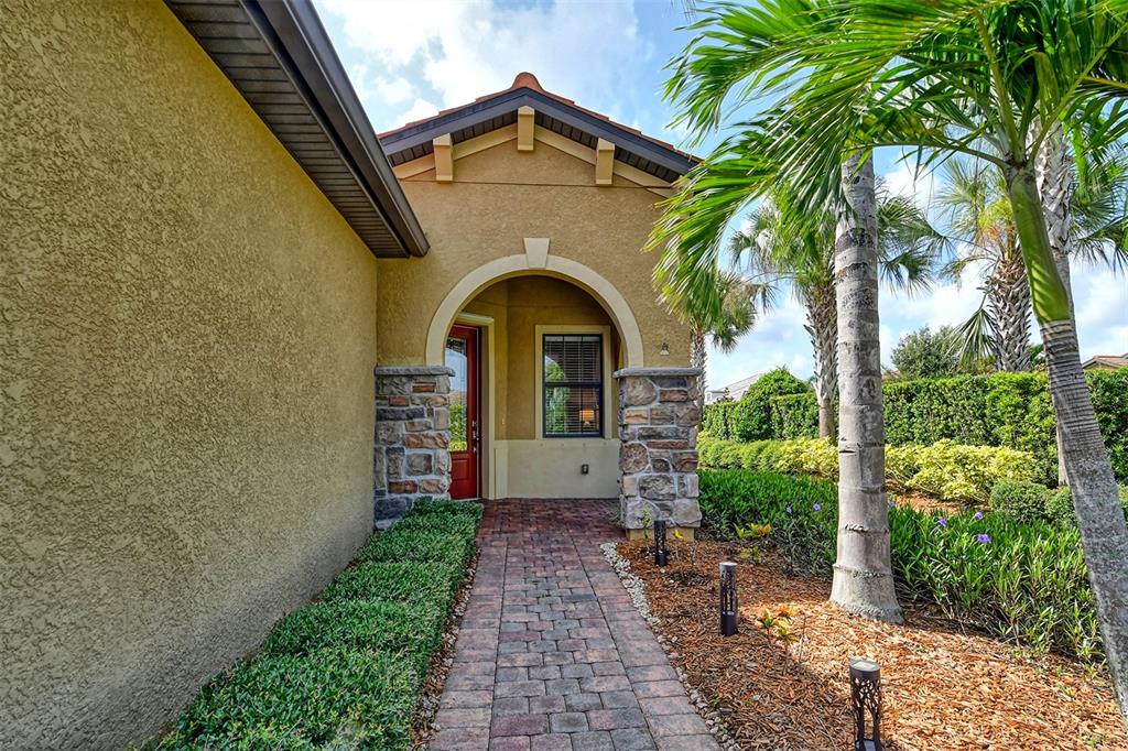 A paved walkway leads to the arched stone-accented entryway of a stucco home — 6743 HAVERHILL COURT, BRADENTON, FL
