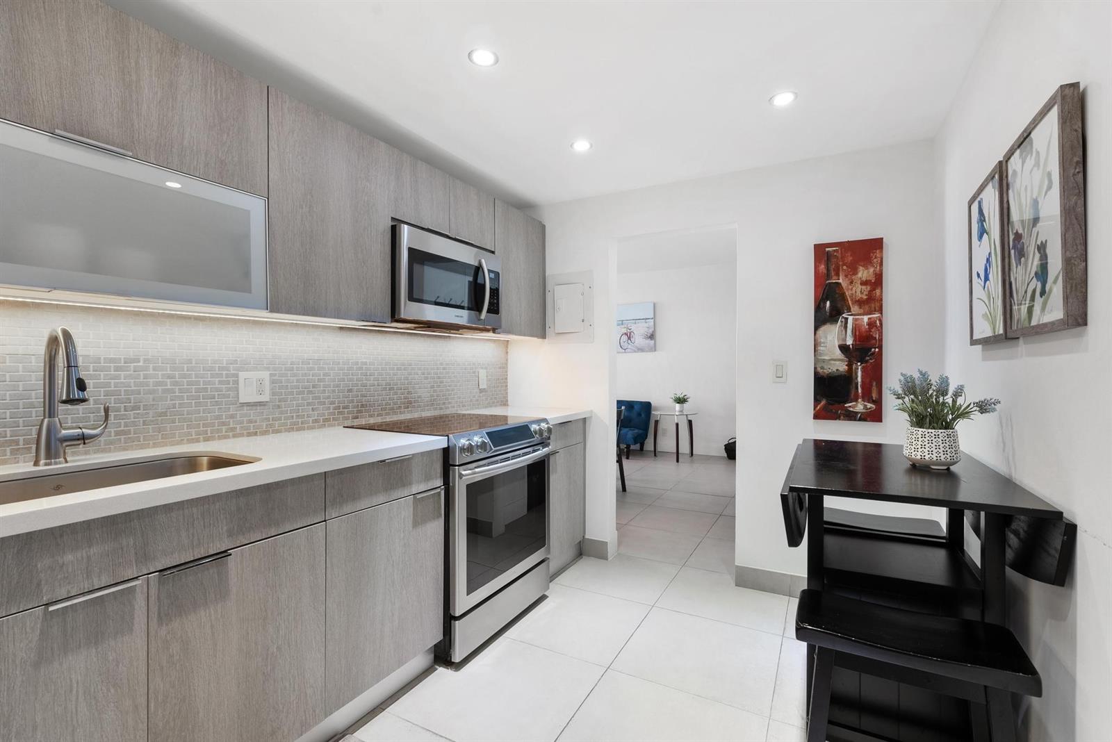 A modern kitchen features gray wood-grain cabinets, stainless steel appliances, and a small dining table — 4001 S Ocean Drive # 8E, Hollywood FL 33019, HOLLYWOOD, FL