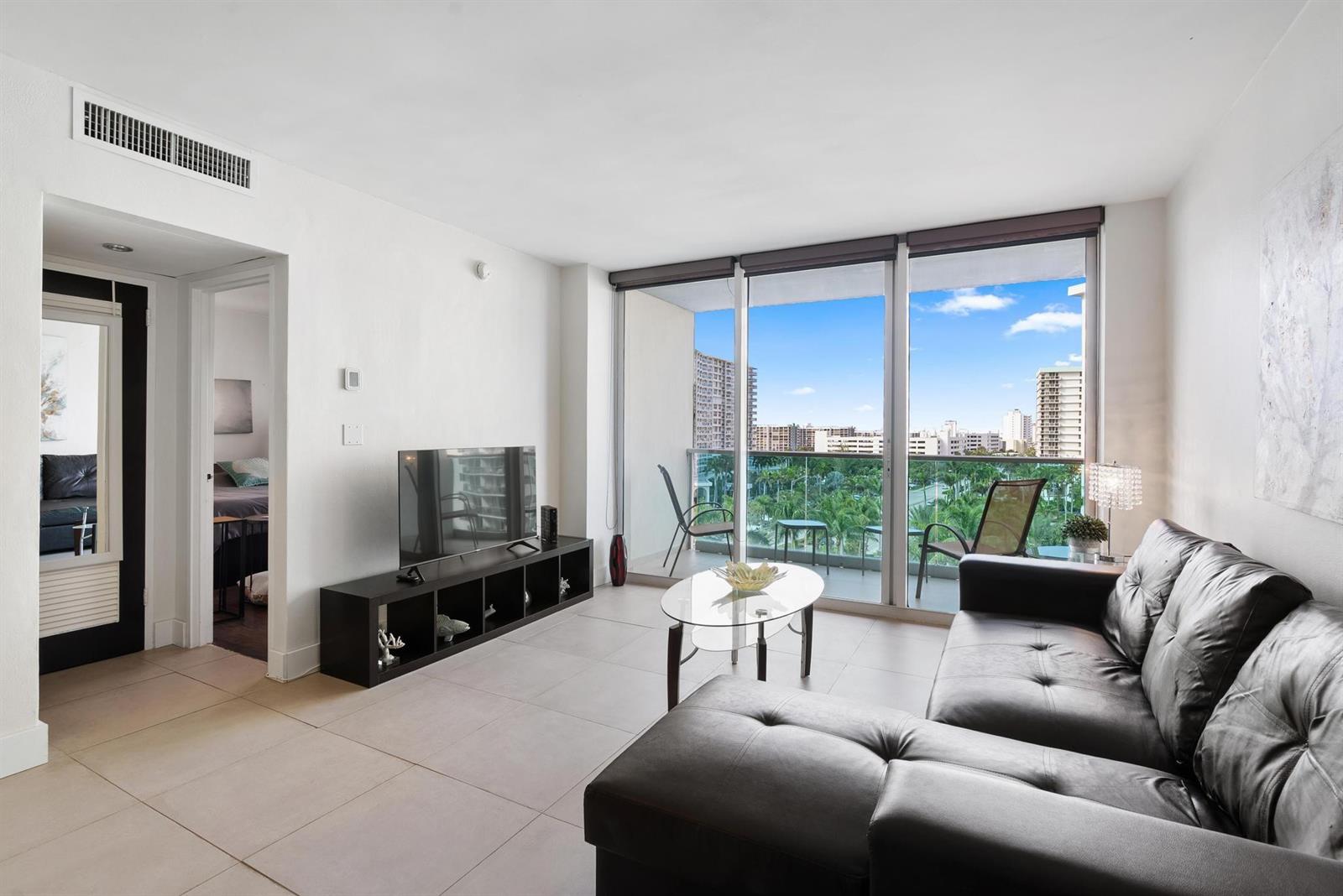 A living room features tile flooring, a black leather sectional, and a balcony with views — 4001 S Ocean Drive # 8E, Hollywood FL 33019, HOLLYWOOD, FL