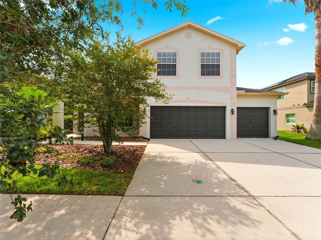 A two-story house with a beige exterior, a three-car garage, and a concrete driveway — 14843 HERONGLEN DRIVE, LITHIA, FL