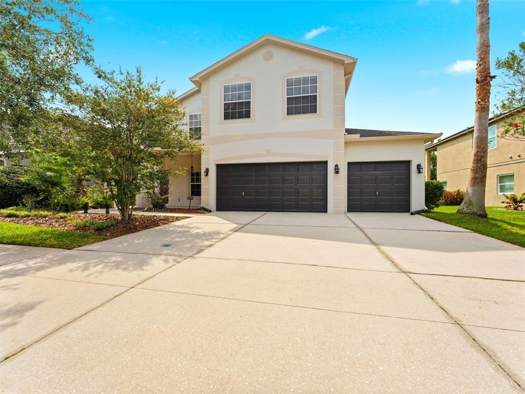 A two-story house with a three-car garage and a concrete driveway under a blue sky — 14843 HERONGLEN DRIVE, LITHIA, FL