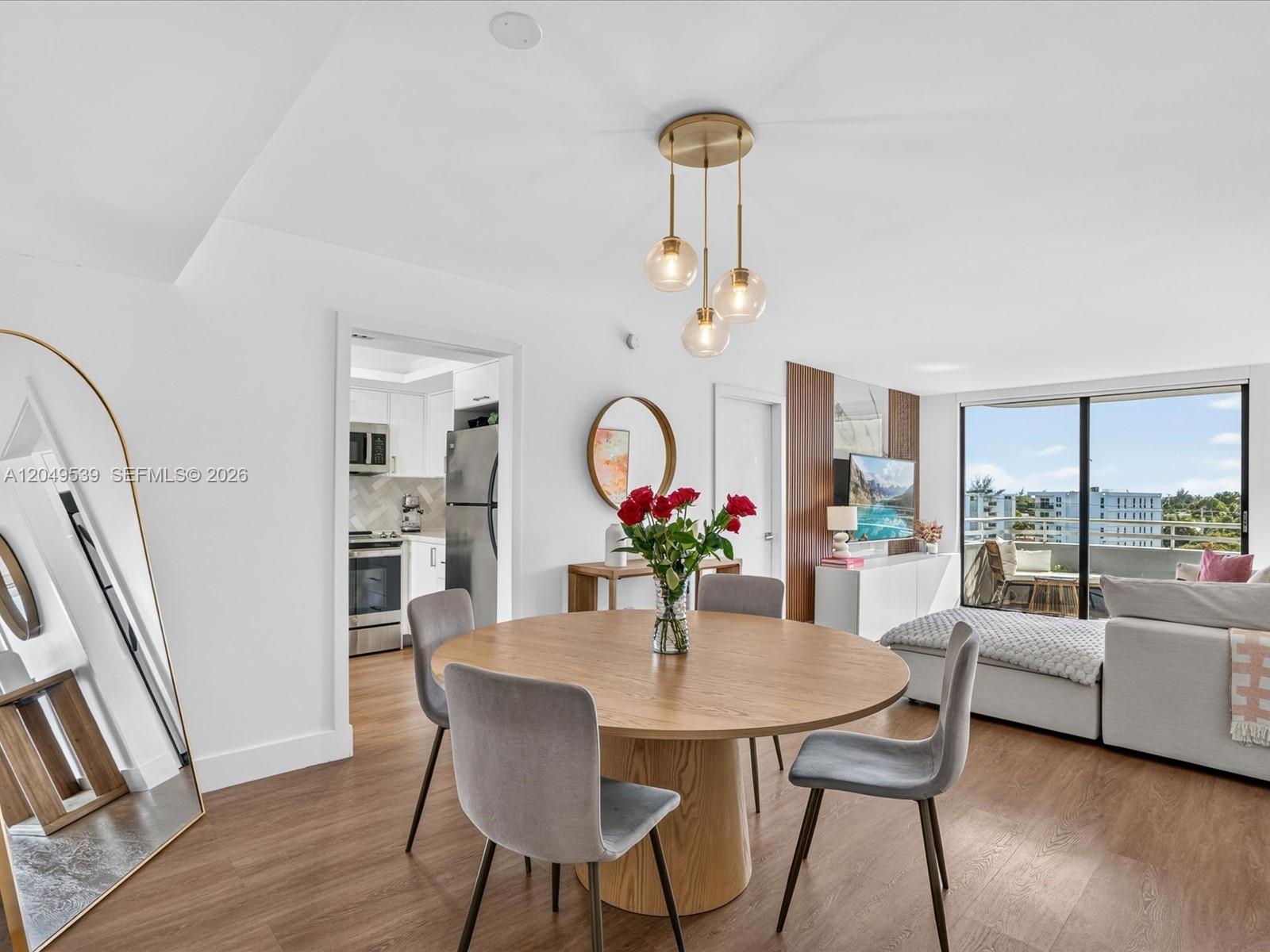 A dining area with a round wooden table leads into a living room with balcony access — 8201 Byron Ave # 502, Miami Beach FL 33141, MIAMI BEACH, FL