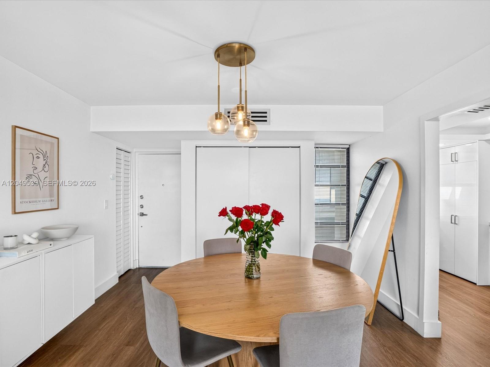 A dining area features a round wooden table, grey chairs, and a modern pendant light — 8201 Byron Ave # 502, Miami Beach FL 33141, MIAMI BEACH, FL