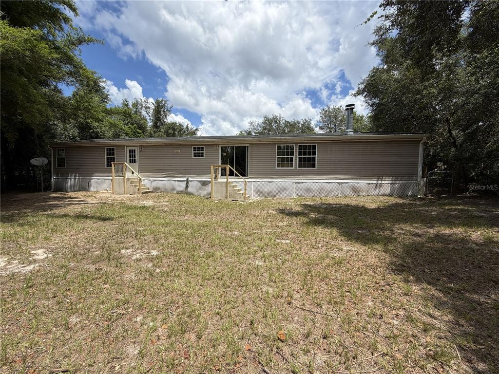 The exterior of a single-story manufactured home features beige siding, lattice skirting, and two wooden staircases — 41527 PARADISE ROAD, DELAND, FL