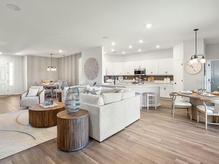 An open-concept living room, dining area, and kitchen with white cabinetry and wood-look flooring — 8687 WILDFLOWER FIELDS LANE, WILDWOOD, FL
