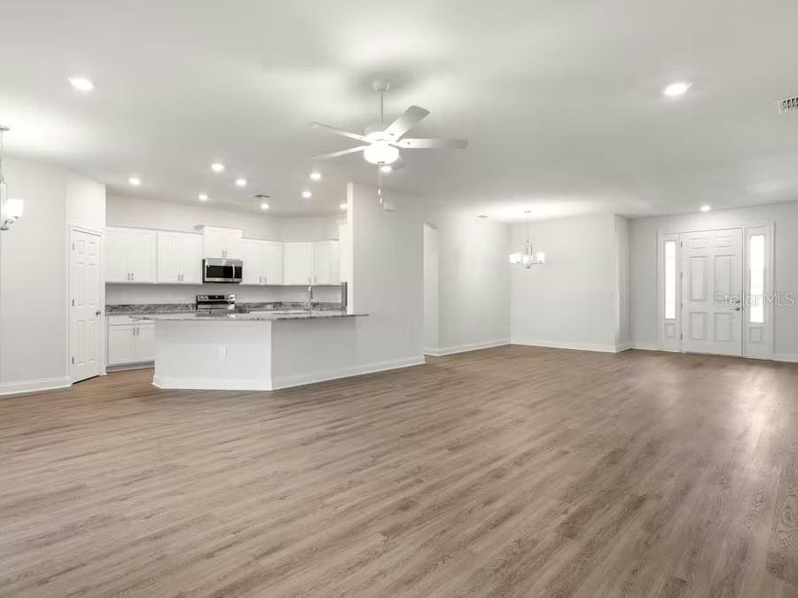 An open-concept kitchen and living area with white cabinets, granite countertops, and wood-look flooring — 8687 WILDFLOWER FIELDS LANE, WILDWOOD, FL