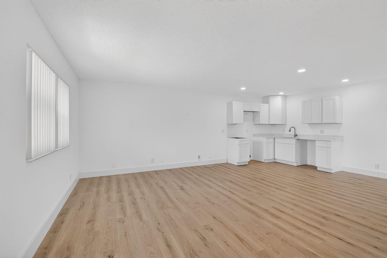 An open-concept room features white walls, light wood-look flooring, and a small white kitchen — 155 Seville G, Delray Beach FL 33446, DELRAY BEACH, FL