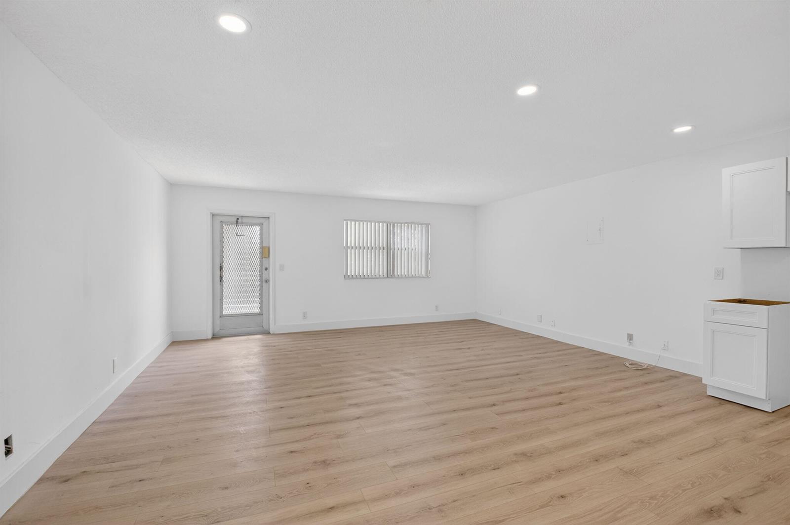 An empty room with light wood-look flooring, white walls, recessed lighting, and a kitchen cabinet — 155 Seville G, Delray Beach FL 33446, DELRAY BEACH, FL
