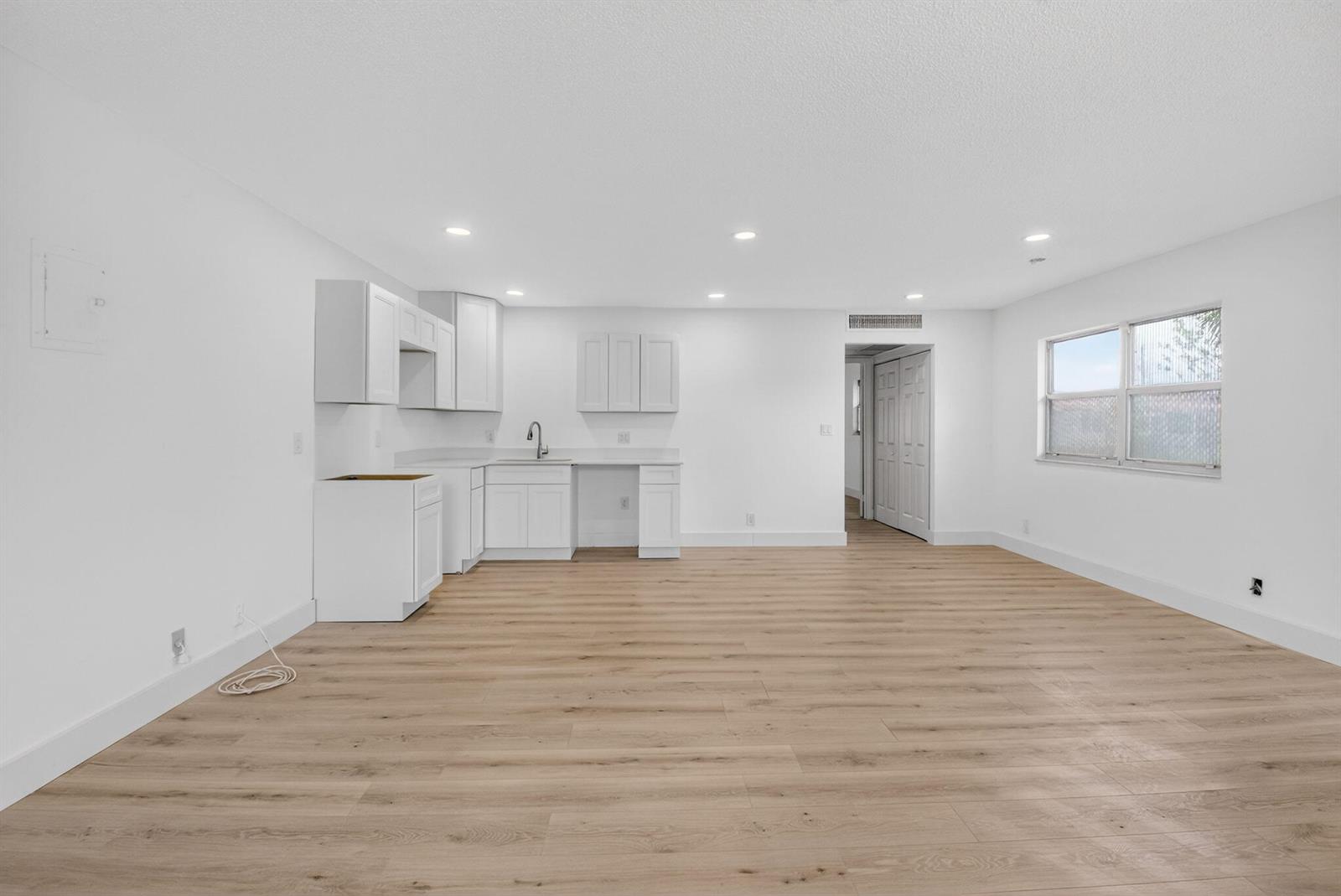 A bright, open-concept kitchen and living area features white cabinetry and light wood flooring — 155 Seville G, Delray Beach FL 33446, DELRAY BEACH, FL