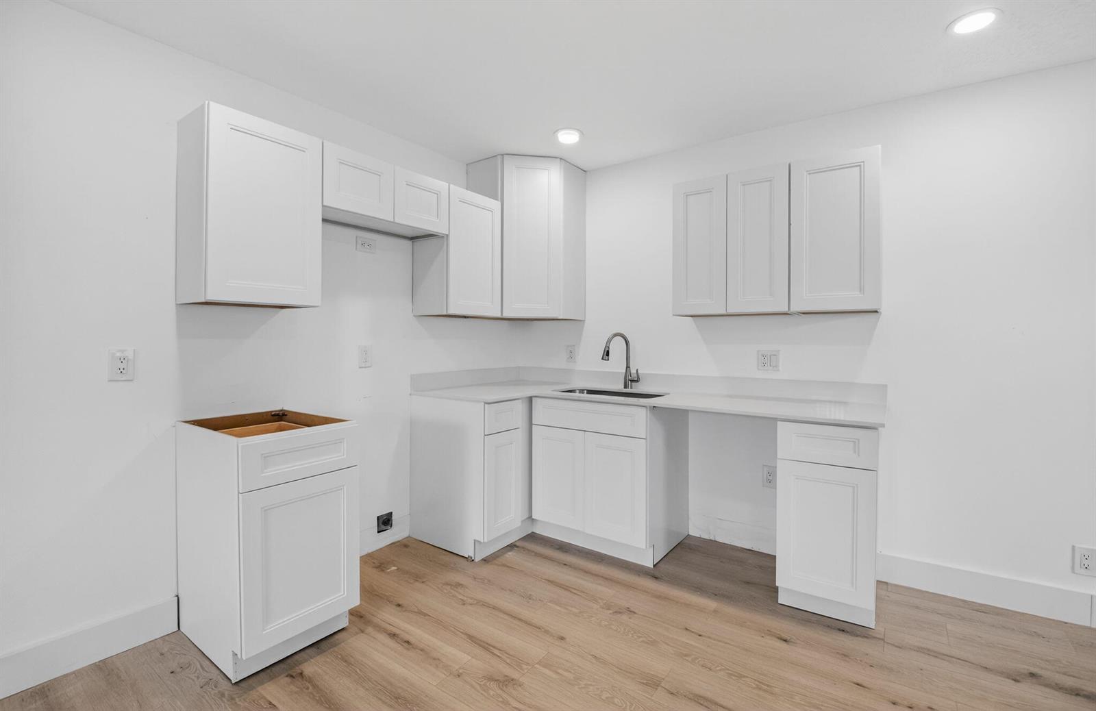 A kitchen features white cabinets, light countertops, a stainless steel sink, and wood-look flooring — 155 Seville G, Delray Beach FL 33446, DELRAY BEACH, FL