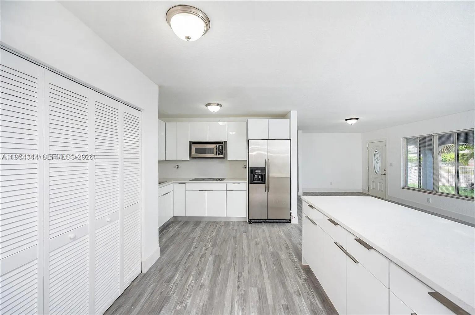 A modern kitchen features white cabinetry, stainless steel appliances, and gray wood-look flooring — 11950 SW 182nd Ter, Miami FL 33177, MIAMI, FL