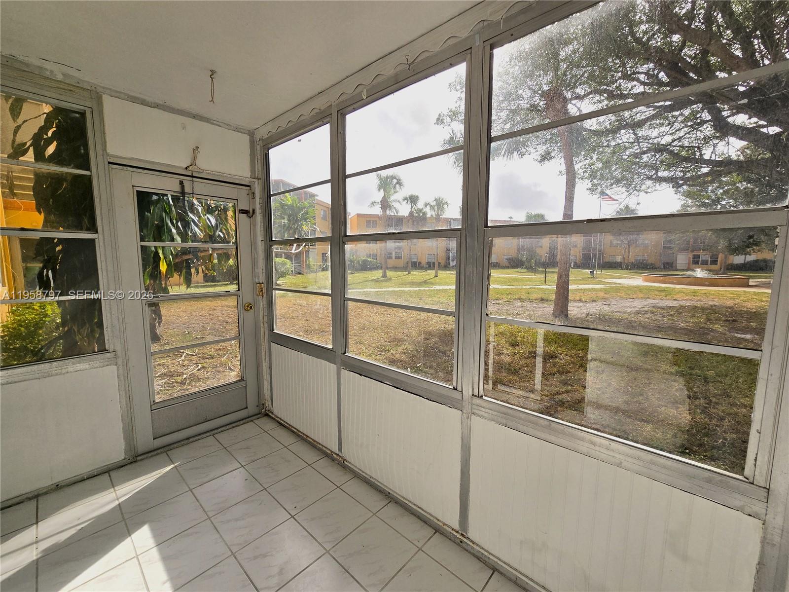 A sunroom with white tiled flooring, aluminum-framed windows, and a screen door overlooking a courtyard — 4334 NW 9th Ave # 1B, Deerfield Beach FL 33064, DEERFIELD BEACH, FL