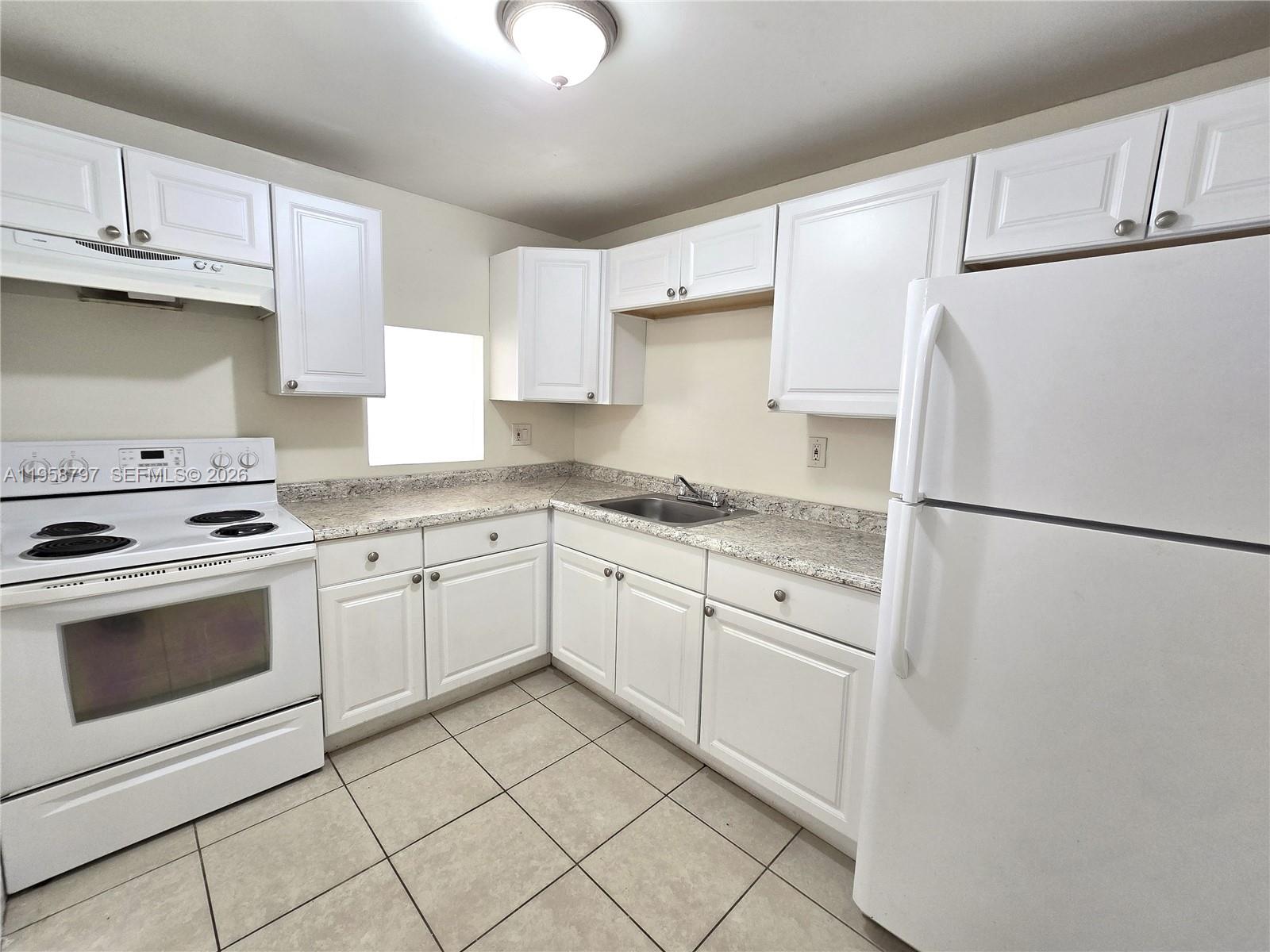 A kitchen features white cabinets, white appliances, speckled countertops, and light-colored tile flooring — 4334 NW 9th Ave # 1B, Deerfield Beach FL 33064, DEERFIELD BEACH, FL