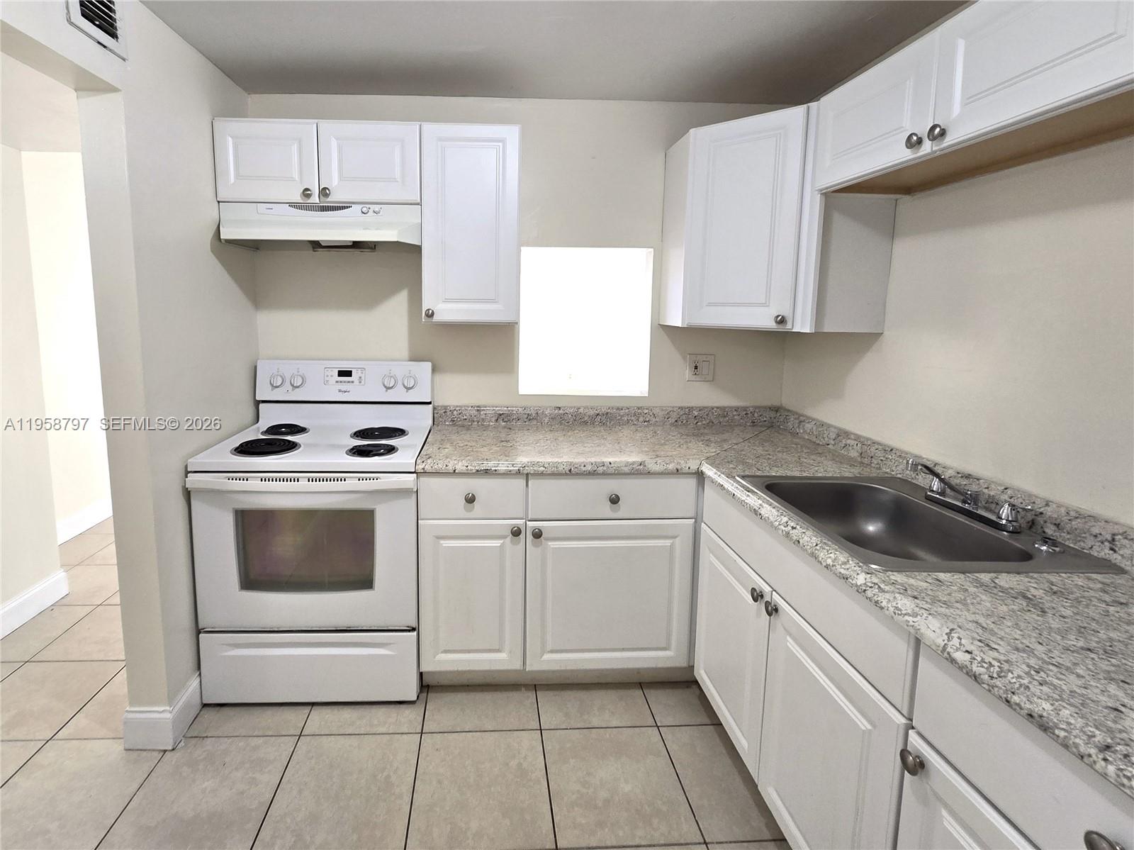A kitchen features white cabinets, granite countertops, a white stove, and a stainless steel sink — 4334 NW 9th Ave # 1B, Deerfield Beach FL 33064, DEERFIELD BEACH, FL