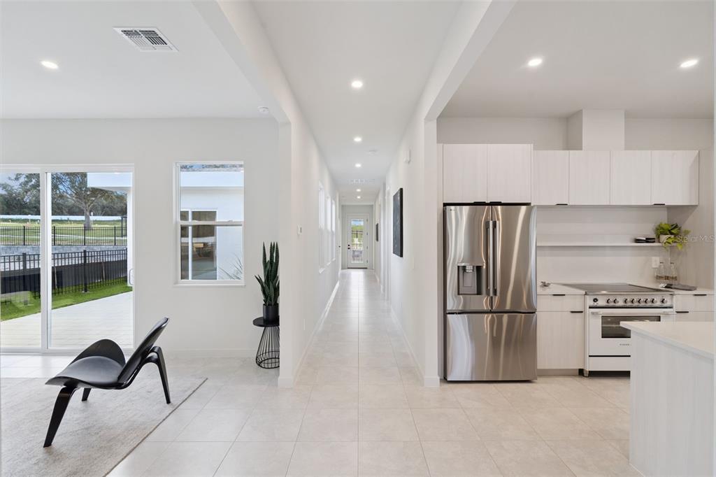 A bright kitchen and hallway feature white cabinetry, stainless steel appliances, and light tile flooring — 438 SKYFIELD COURT, LADY LAKE, FL