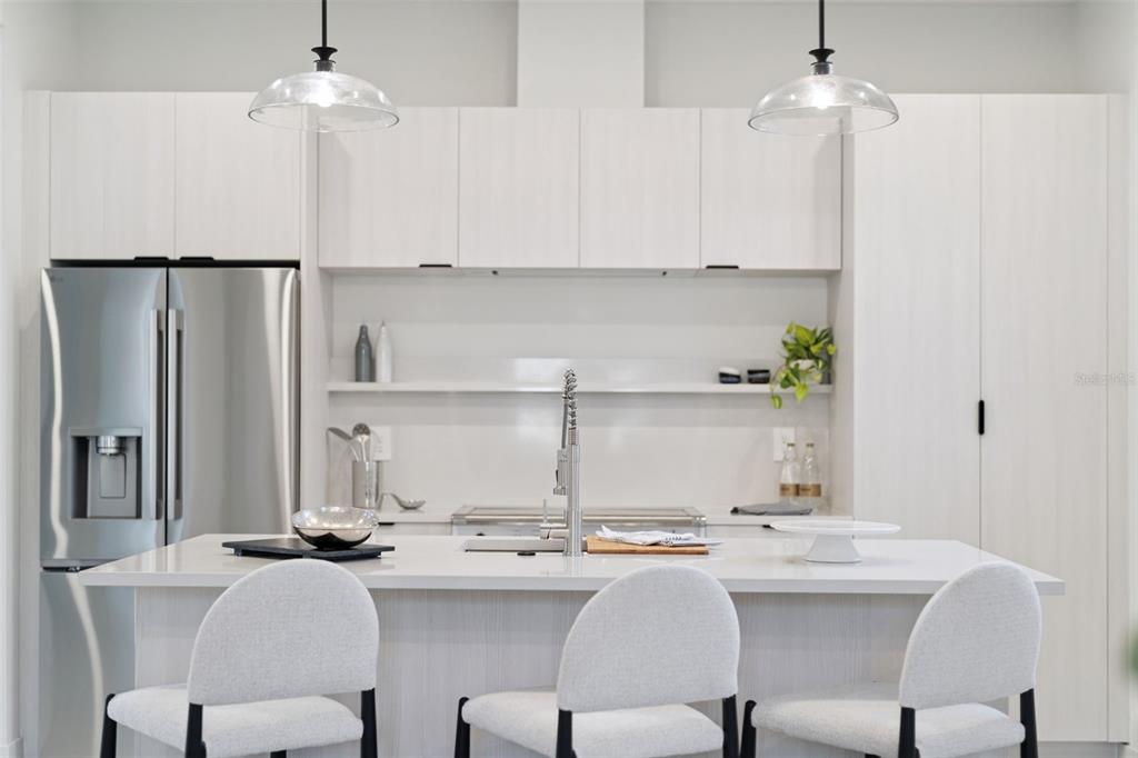 A modern kitchen features white cabinetry, a stainless steel refrigerator, and a central island — 438 SKYFIELD COURT, LADY LAKE, FL