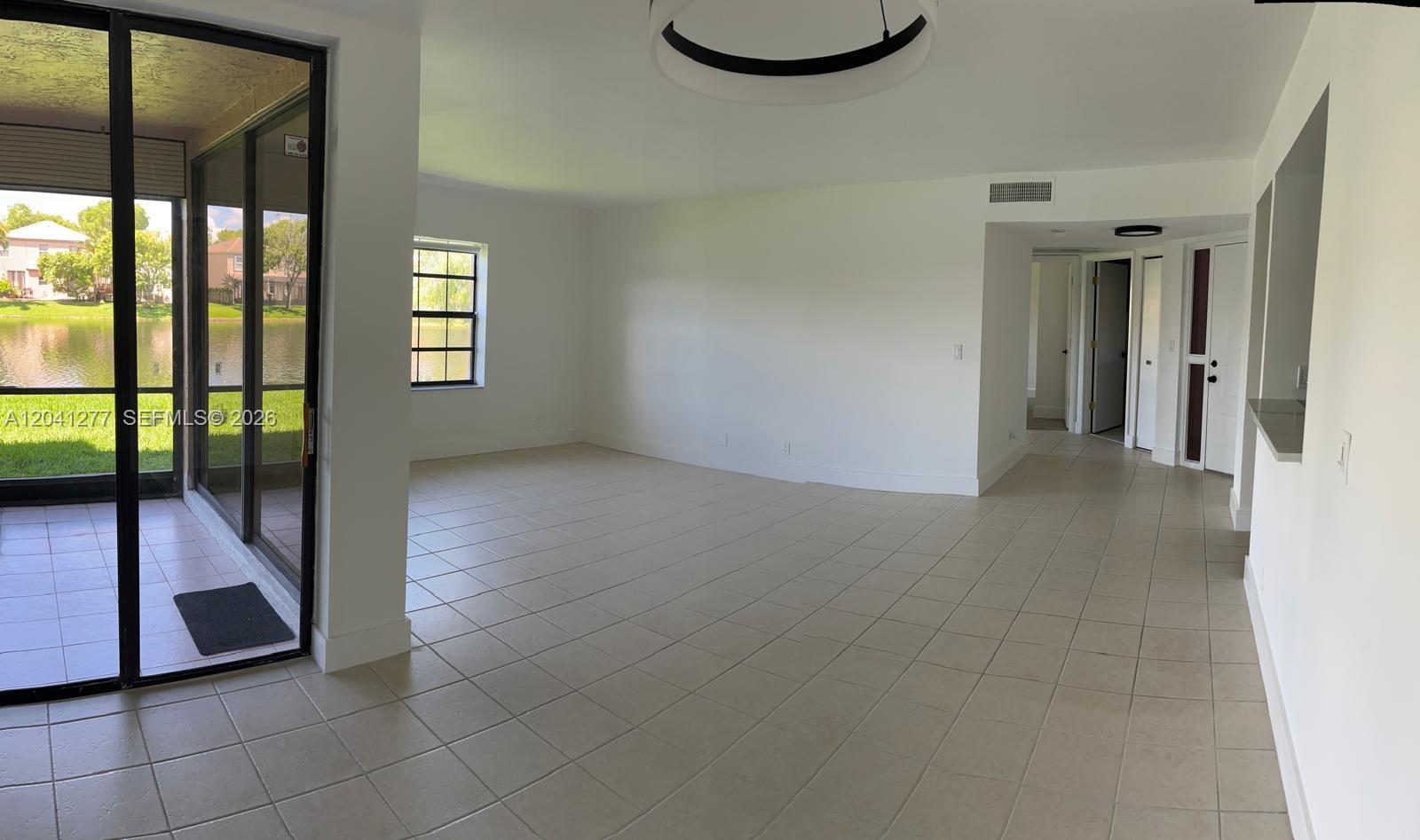 A bright living room features light tile flooring, white walls, and a sliding glass door — PLANTATION, FL