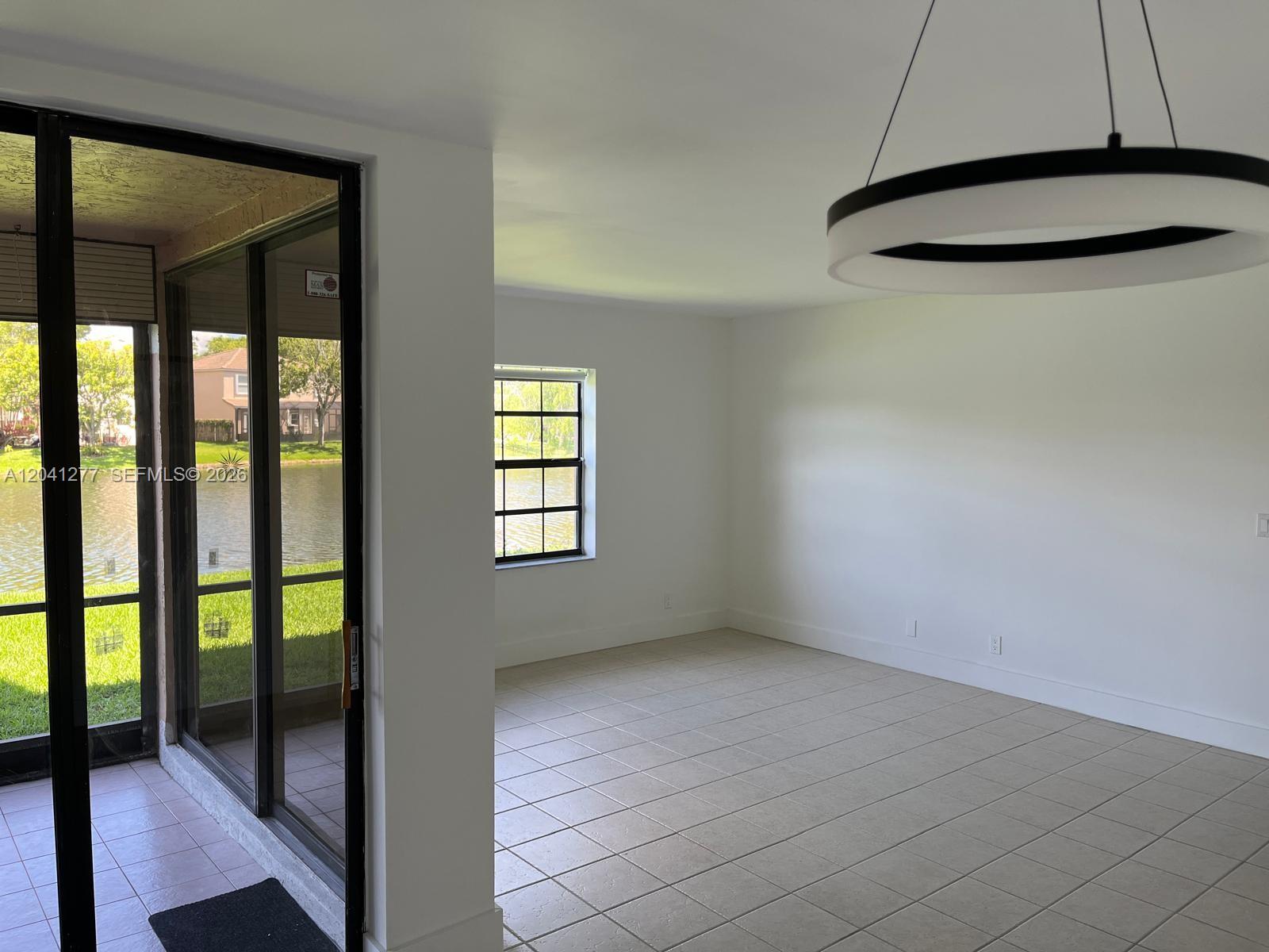 An empty room with tiled floors, white walls, a modern circular light, and a sliding door — PLANTATION, FL