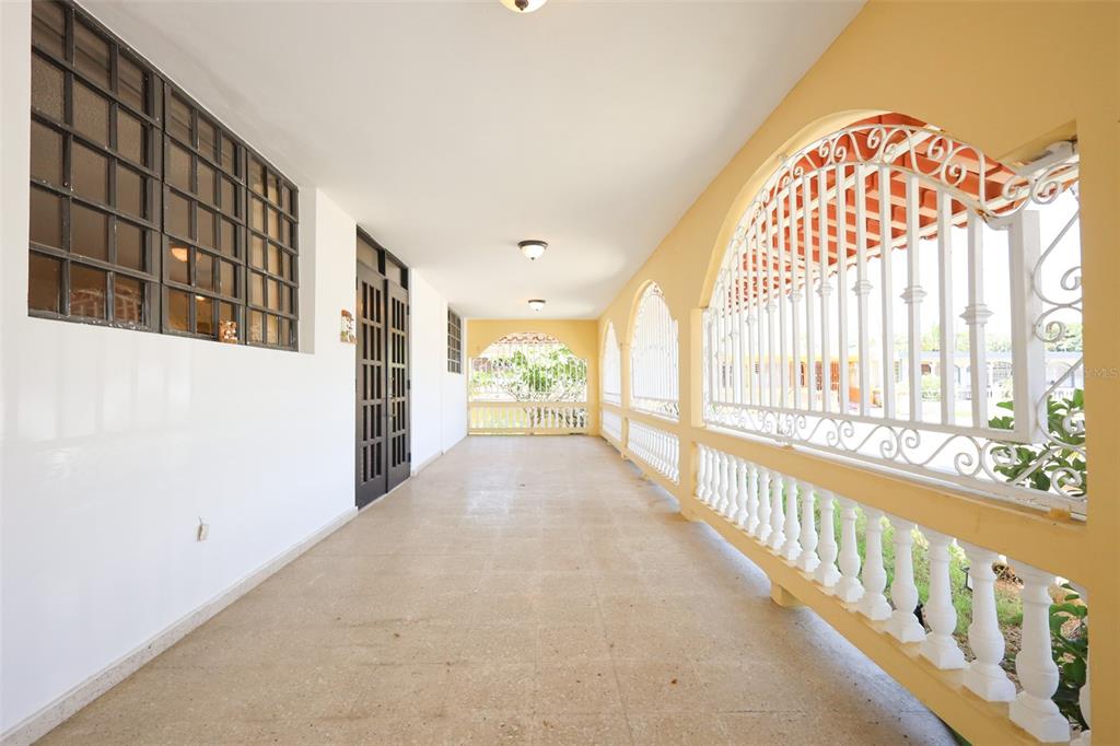 A long, covered outdoor porch features a tiled floor, white walls, and decorative metal railings — D-1 HATILLO DEL MAR, HATILLO, PR