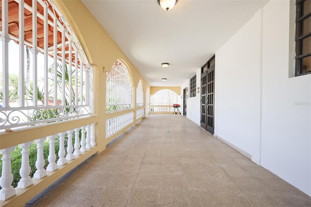 A long, covered outdoor porch features white balustrades, arched metal railings, and tiled flooring — D-1 HATILLO DEL MAR, HATILLO, PR