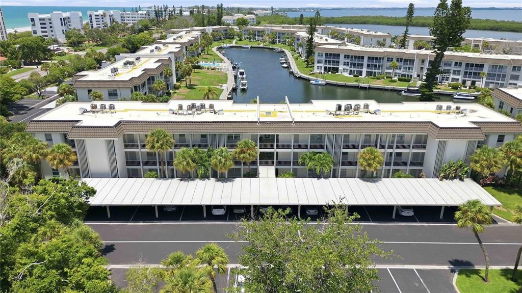 An aerial view shows a multi-story apartment building with a covered parking area and canal — 4340 FALMOUTH DRIVE UNIT 104, LONGBOAT KEY, FL