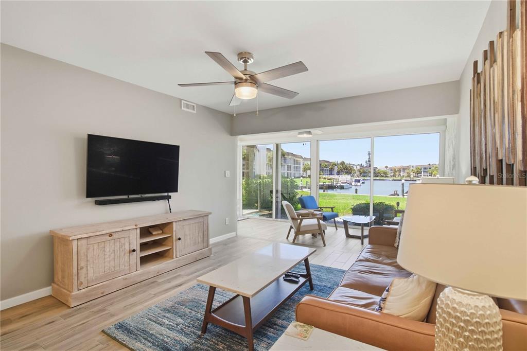 A living room features a leather sofa, wood media console, and sliding doors overlooking a canal — 4340 FALMOUTH DRIVE UNIT 104, LONGBOAT KEY, FL