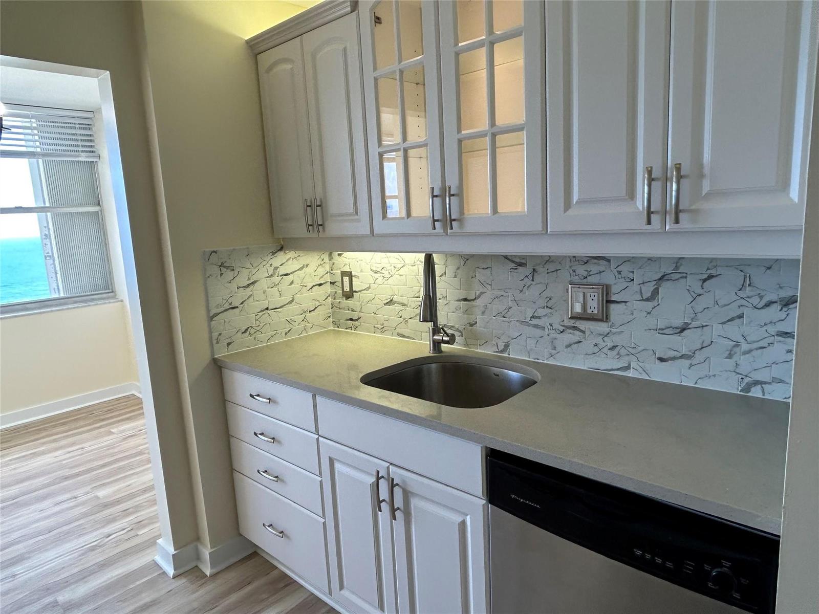 A kitchen features white cabinets, a marble-patterned backsplash, a stainless steel sink, and a dishwasher — 111 Briny Avenue # 1401, Pompano Beach FL 33062, POMPANO BEACH, FL