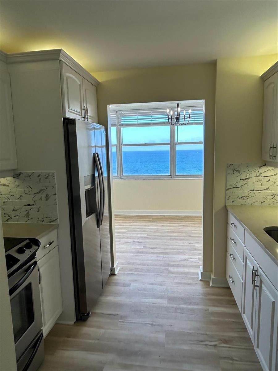 A kitchen with white cabinets and marble-look backsplash opens to a room with ocean views — 111 Briny Avenue # 1401, Pompano Beach FL 33062, POMPANO BEACH, FL