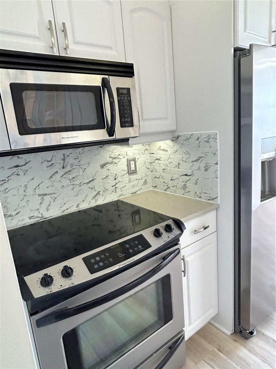 A kitchen features stainless steel appliances, white cabinets, and a marble-patterned tile backsplash — 111 Briny Avenue # 1401, Pompano Beach FL 33062, POMPANO BEACH, FL