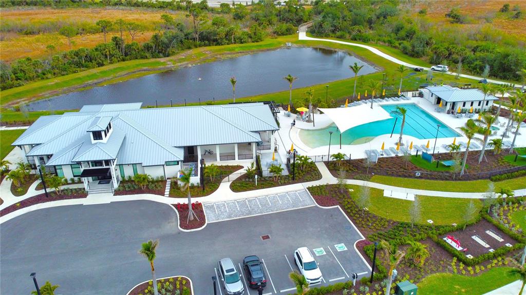 An aerial view shows a community clubhouse with a swimming pool, parking lot, and pond — 17784 STILLNESS COURT, VENICE, FL