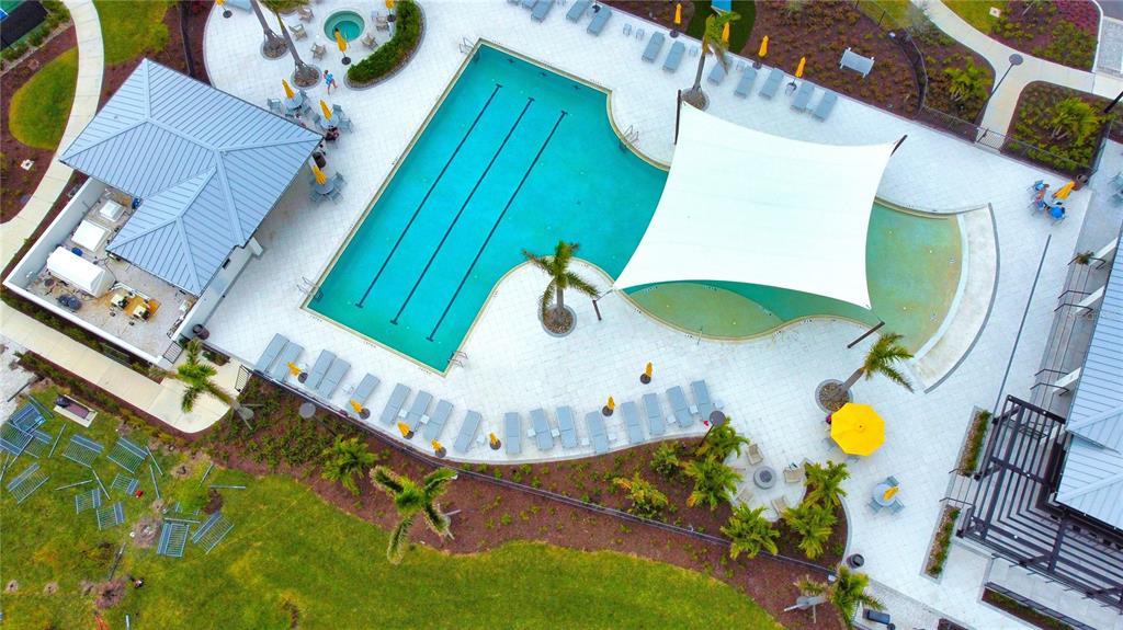 An aerial view shows a swimming pool with a shade sail, lounge chairs, and building — 17784 STILLNESS COURT, VENICE, FL
