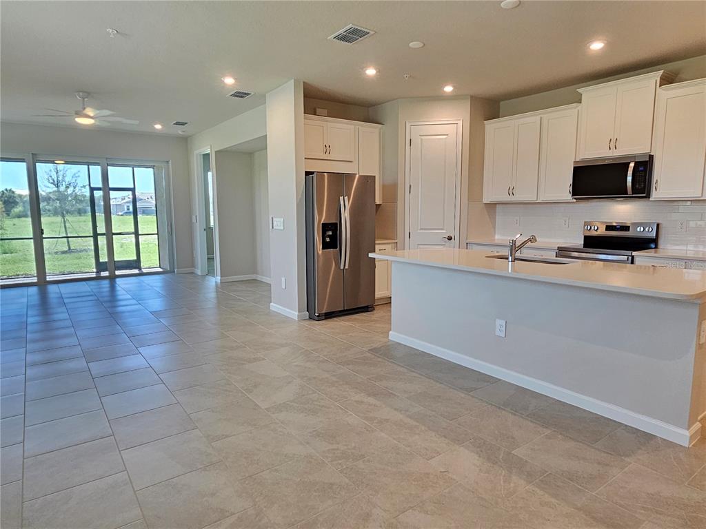 A kitchen with white cabinets, stainless steel appliances, and tile flooring opens to a living area — 17784 STILLNESS COURT, VENICE, FL