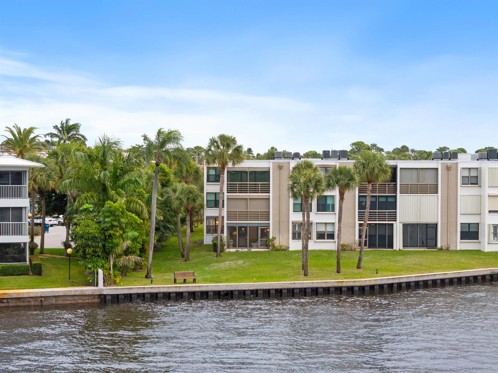 An exterior view of a multi-story apartment building situated along a canal with palm trees — 1950 SW Palm City Road # 107, Stuart FL 34994, STUART, FL