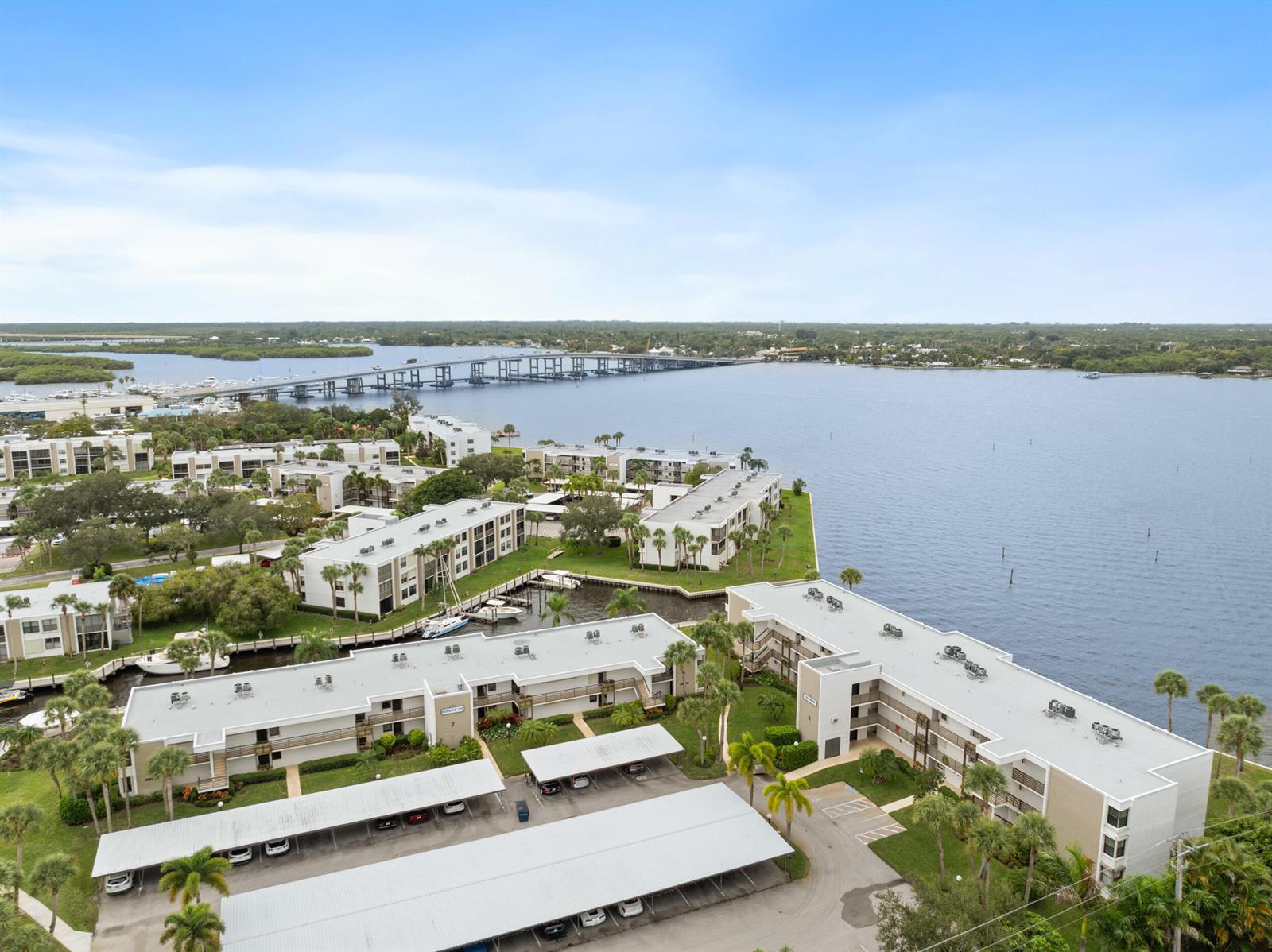 An aerial view shows multiple apartment buildings with covered parking lots near a large bay — 1950 SW Palm City Road # 107, Stuart FL 34994, STUART, FL