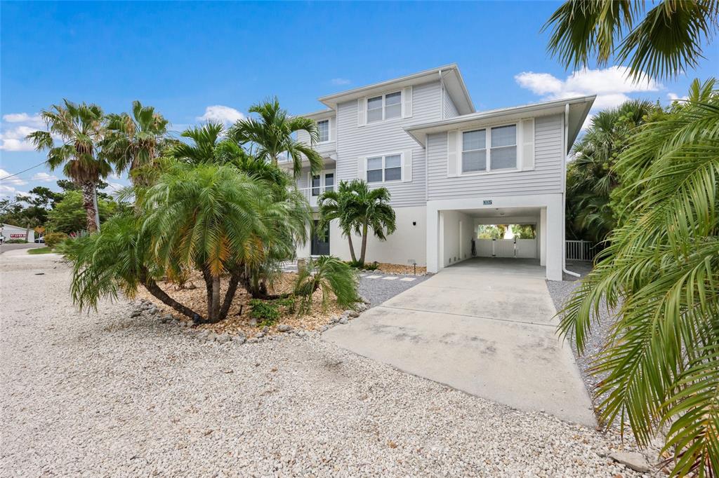 A three-story light gray house with a concrete driveway and palm trees in the front — 115 HAMMOCK ROAD, ANNA MARIA, FL