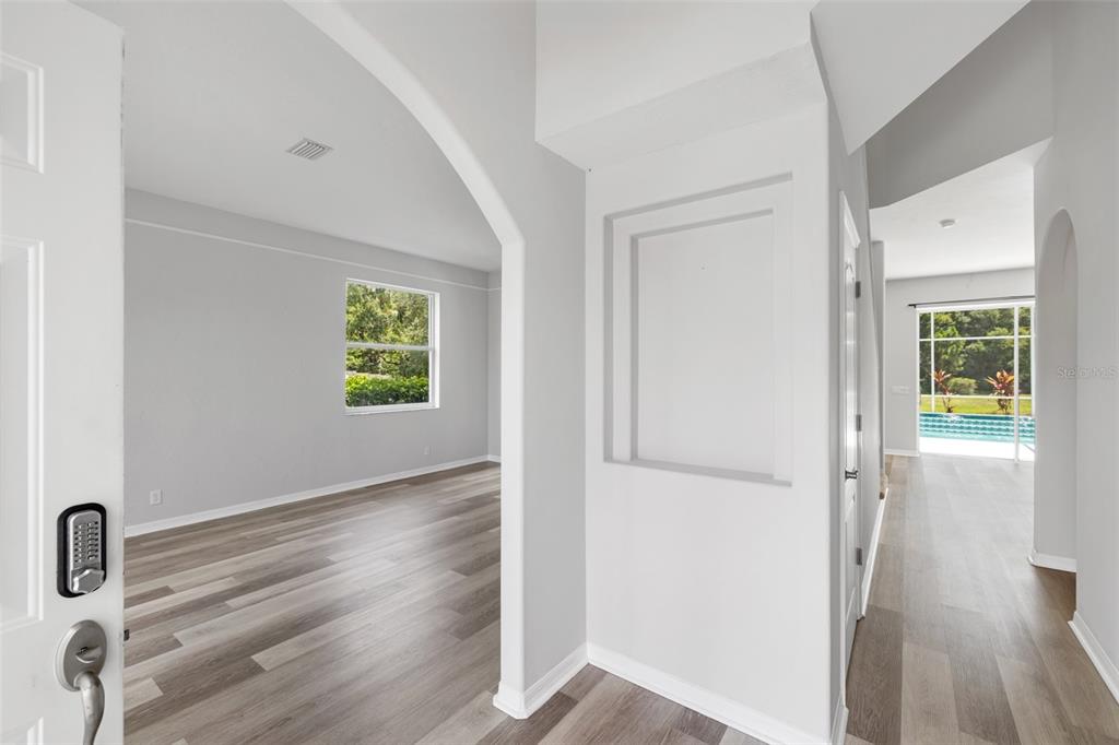 An entryway with light wood-look flooring leads to an arched room and a pool view — 4705 78TH COURT E, BRADENTON, FL