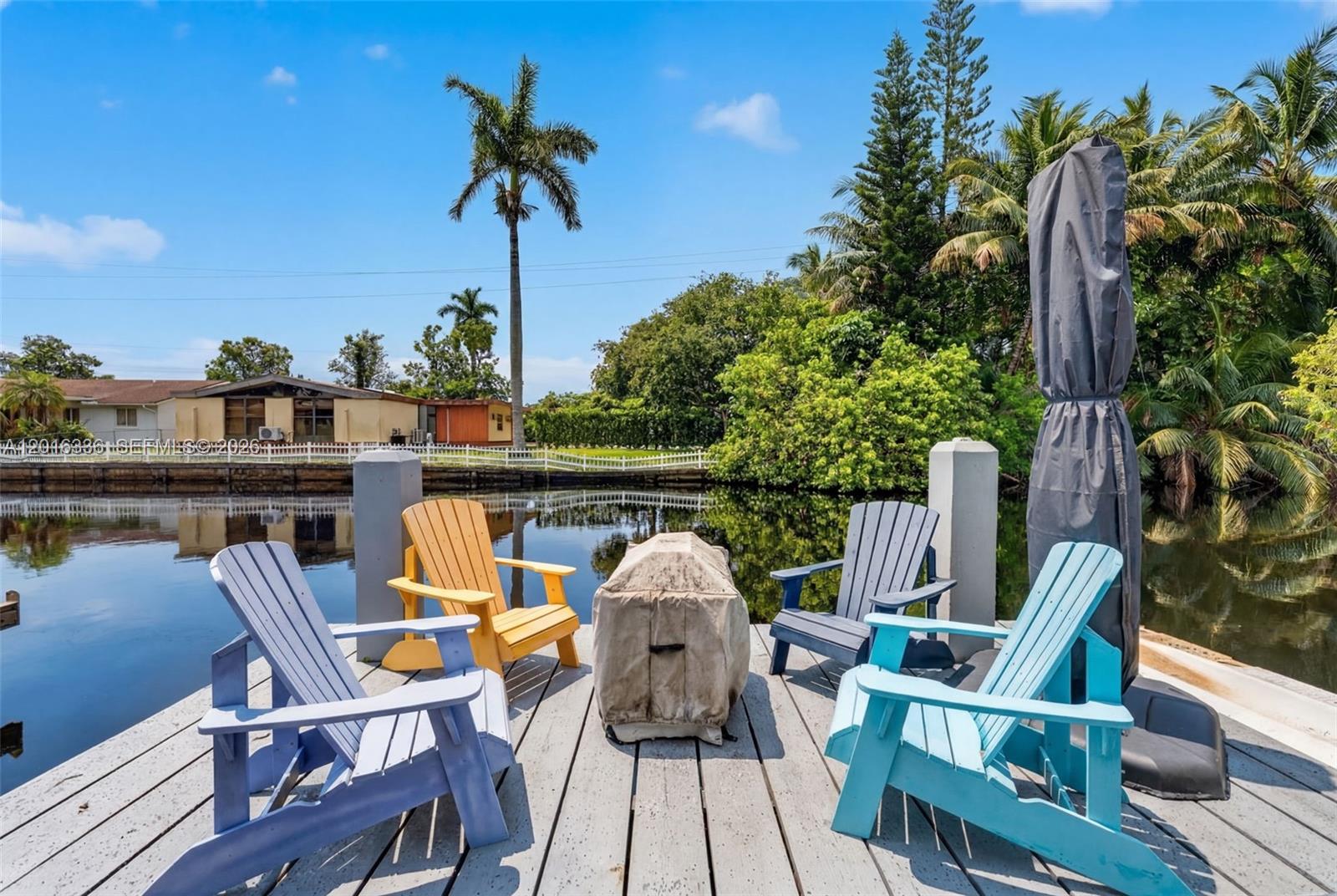 Four colorful Adirondack chairs surround a covered fire pit on a wooden dock by water — 2918 Cleveland St, Hollywood FL 33020, HOLLYWOOD, FL