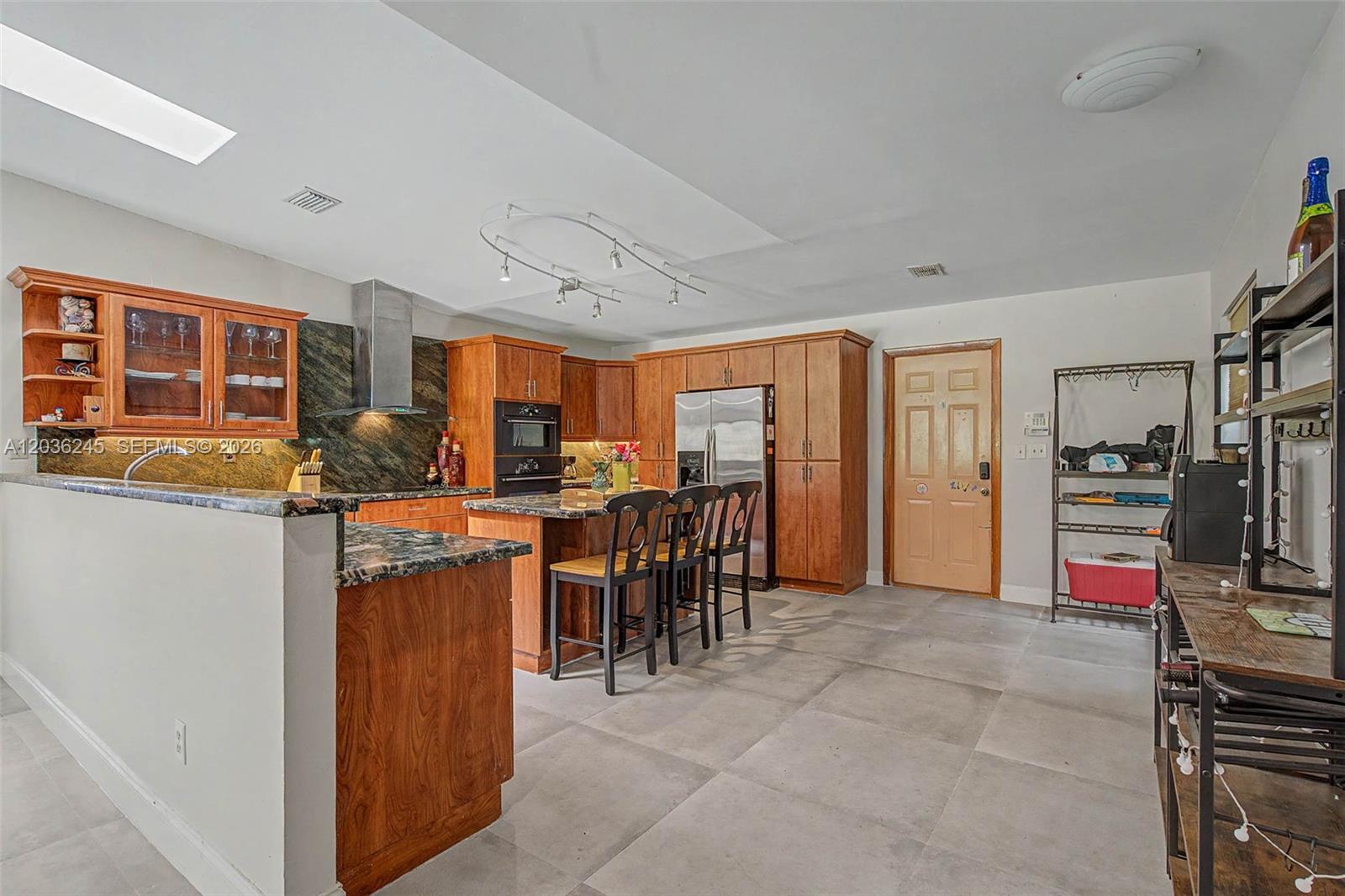 A kitchen features wood cabinets, dark granite countertops, a stainless steel refrigerator, and tile flooring — 15741 SW 147th Ct, Miami FL 33187, MIAMI, FL