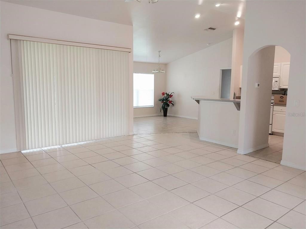A bright, open-concept living area features light-colored floor tiles, a sliding glass door, and an archway — 1695 GAUGUIN ROAD, NORTH PORT, FL