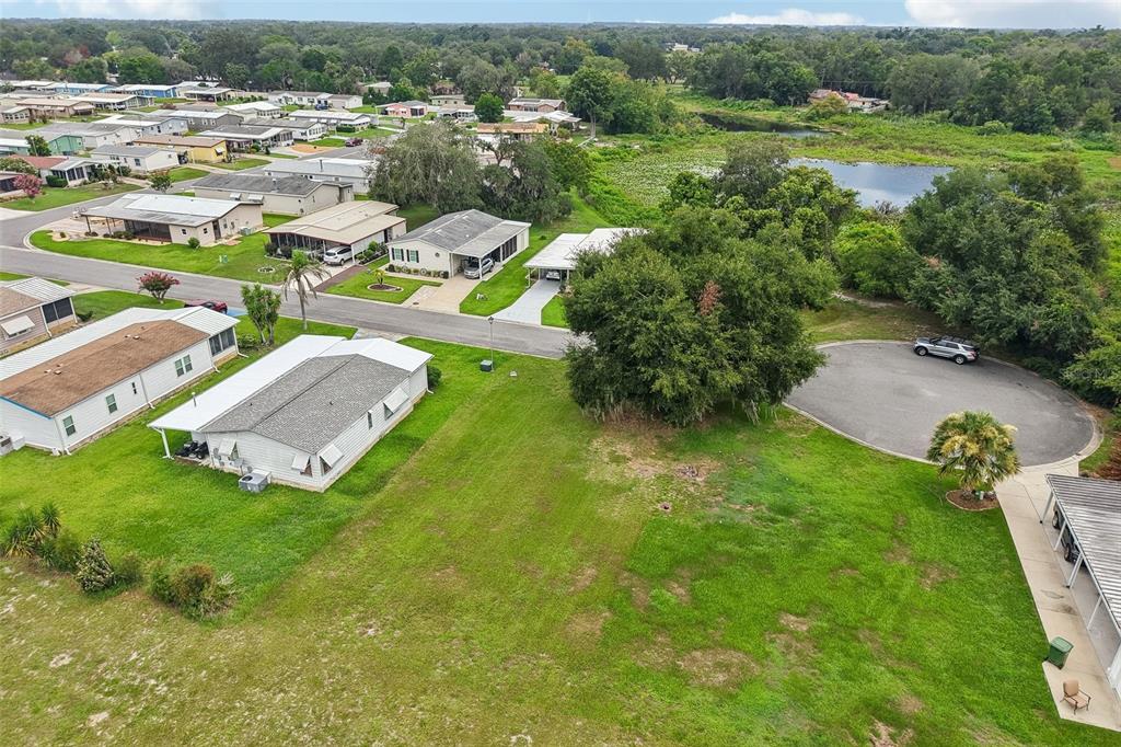 An aerial view shows a residential neighborhood with houses, a grassy lot, and a pond — 2341 W COACH N FOUR DRIVE, LEESBURG, FL