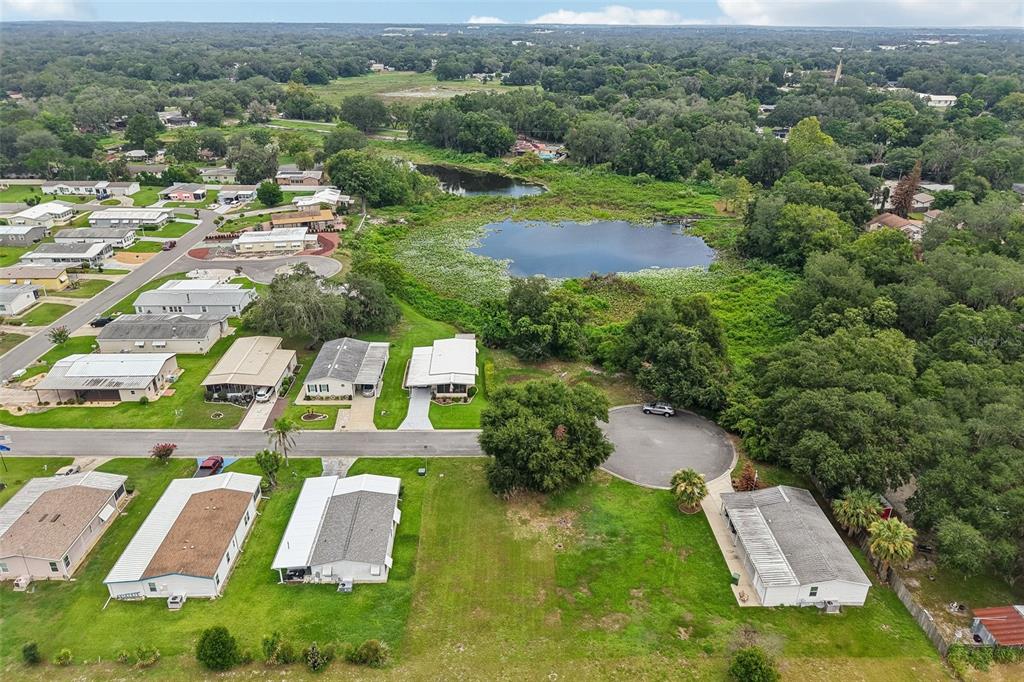 An aerial view shows a residential neighborhood with mobile homes, a pond, and surrounding trees — 2341 W COACH N FOUR DRIVE, LEESBURG, FL