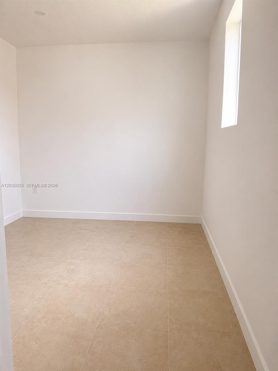 An empty room features light-colored tile flooring, white walls, and a single vertical window — 11931 SW 132nd Ave, Miami FL 33186, MIAMI, FL