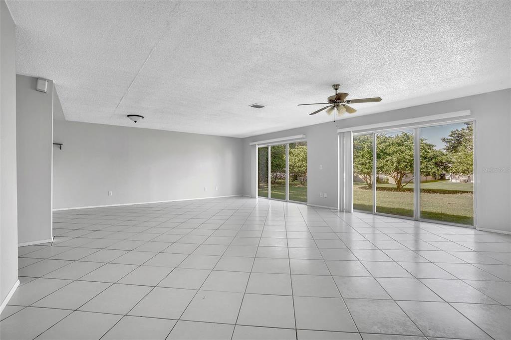 A spacious, empty living room features light gray tile flooring, white walls, and sliding glass doors — 10626 DEERGRASS LANE, ORLANDO, FL
