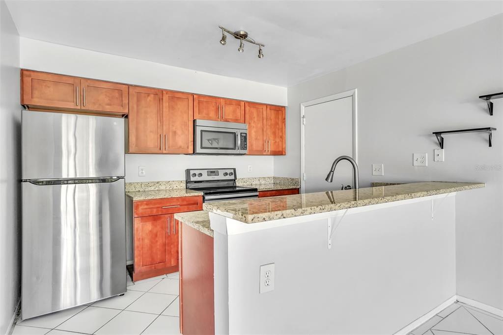 A kitchen features wood cabinets, granite countertops, stainless steel appliances, and a breakfast bar — 10626 DEERGRASS LANE, ORLANDO, FL