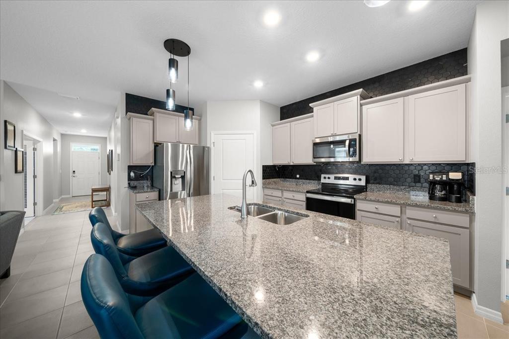 A kitchen features a granite-topped island, blue bar stools, and light gray cabinetry — 5556 NW 41ST LANE, OCALA, FL